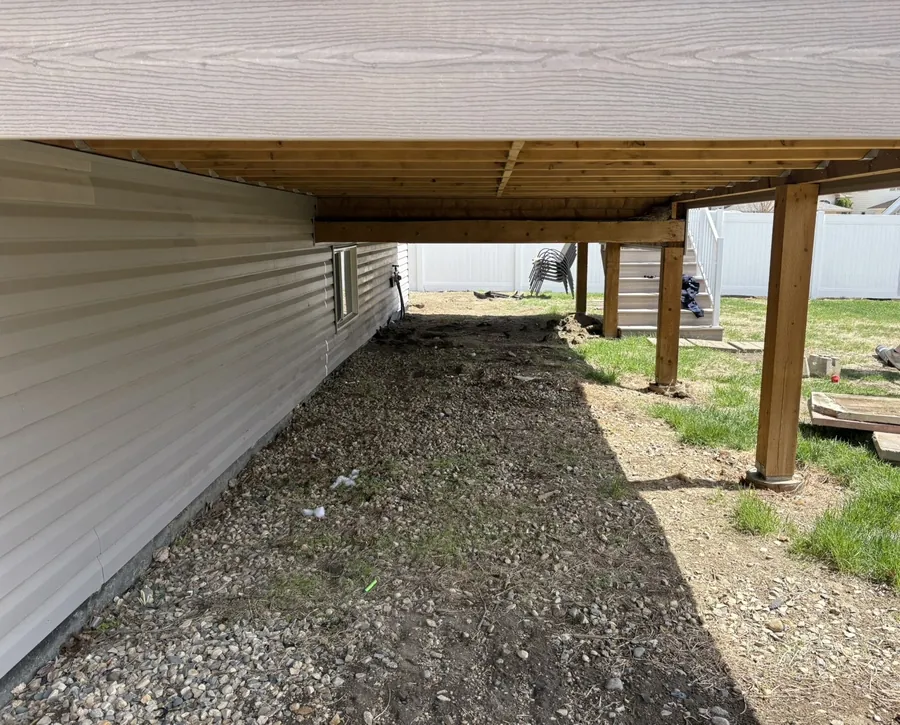Dirt and weeds under a deck before gravel installation in Moose Jaw Saskatchewan